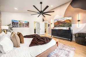 Ein modernes Schlafzimmer mit einem großen Bett, einem Deckenventilator und einem an der Wand befestigten Fernseher.