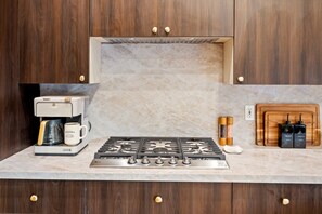 A kitchen with a gas stove, coffee maker, salt and pepper shakers, and a cutting board.