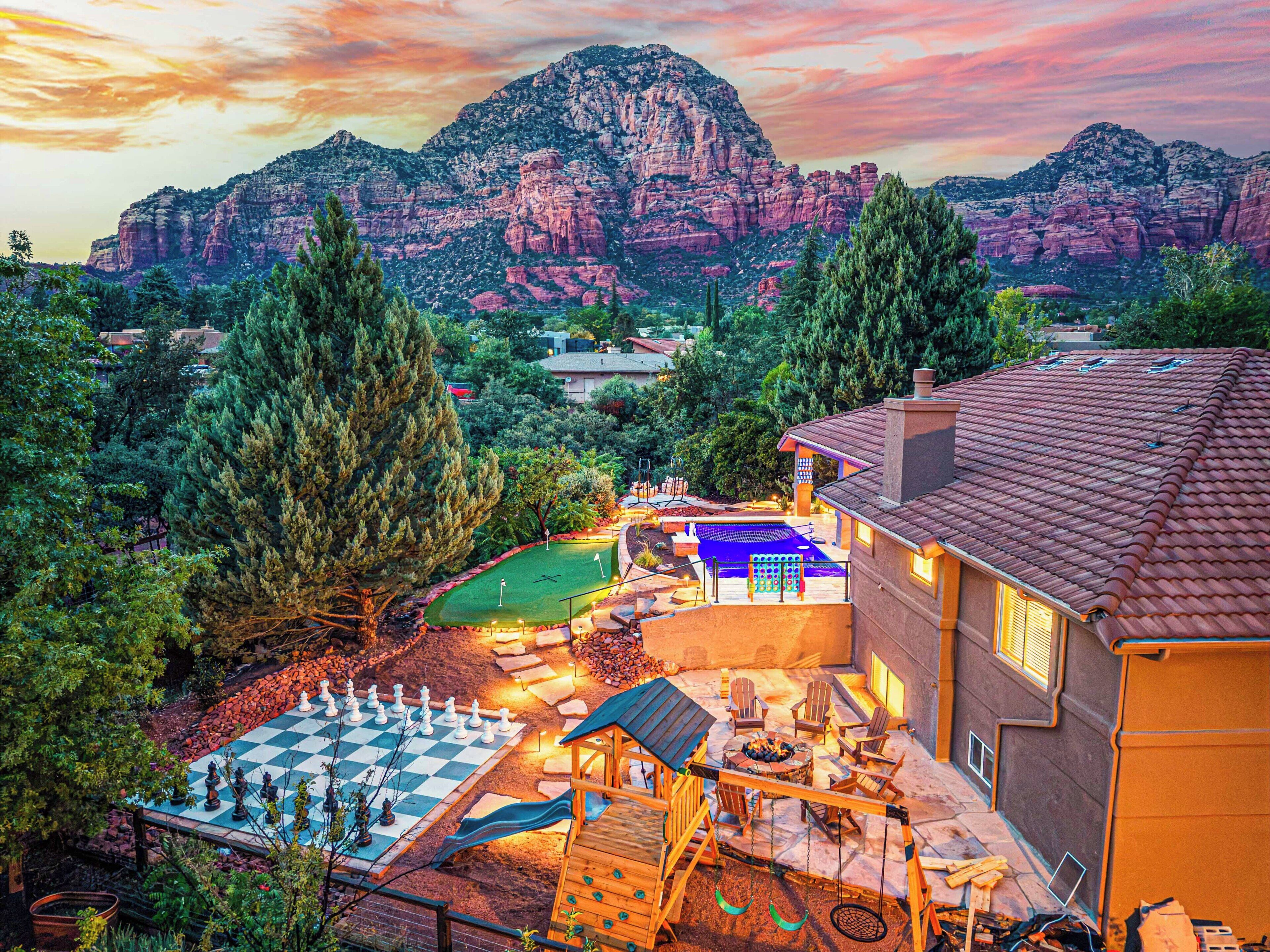 Ein Wohngebiet mit einem großen Berg im Hintergrund, einer gut beleuchteten Terrasse mit Gartenmöbeln und einem Schachbrett.