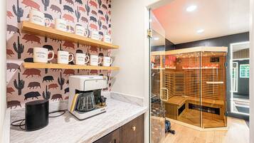 Eine Küche mit Kaffeemaschine, eine Glaskonstruktion mit Sauna sowie eine Wand mit Kaktus- und Wildschweinmuster.