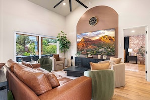 Ein modernes Wohnzimmer mit Ledersofas, einem großen Landschaftsbild und Blick auf Grünflächen.
