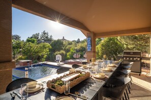 An outdoor dining area with a pool, a basketball hoop, and a grill. - The Yucca House: Pool, Spa, Gym, Theater, Game Room | Epic Red Rock Views (Sedona)