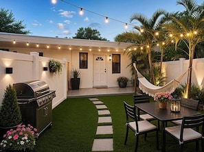 A backyard with a grill, a hammock, a dining table, and string lights. - Renovated 1BR w Private Garden & Laundry (Miami Shores)