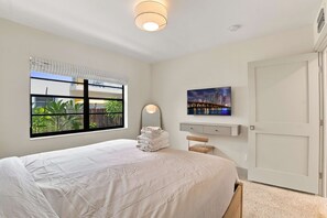 Une chambre à coucher avec un lit, une fenêtre donnant sur un paysage verdoyant, un tableau représentant une vue de la ville et une porte.