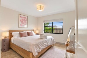 Une chambre à coucher avec un lit en bois, des lampes de chevet, une fenêtre donnant sur un beau paysage et une œuvre d’art encadrée accrochée au mur.