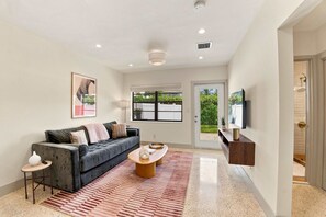 A modern living room with a grey sofa, a coffee table, and a TV mounted on the wall. - Renovated 1BR w Private Garden & Laundry (Miami Shores)