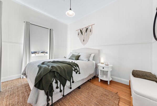 A bedroom with a bed, bedside table, and a hanging macrame wall decoration.