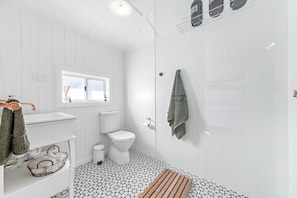 A modern bathroom with a white sink, toilet, and shower. There is a window above the sink and a towel rack on the wall.