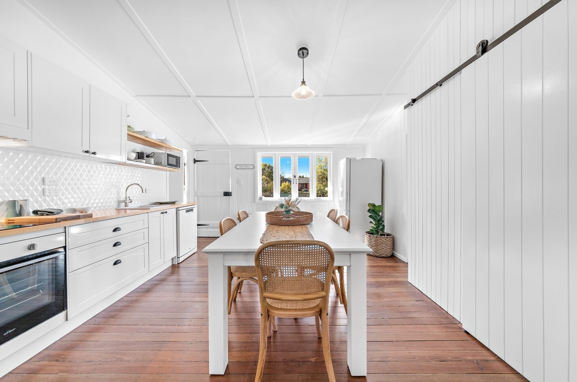 A modern kitchen with white cabinetry, a wooden countertop, and a dining area with a white table and wicker chairs.