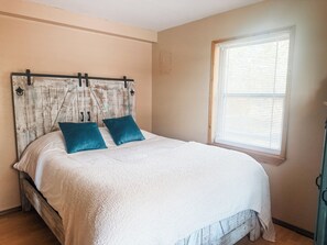 Ein Schlafzimmer mit einem Bett, einem Kopfteil und einem Fenster mit Jalousien.