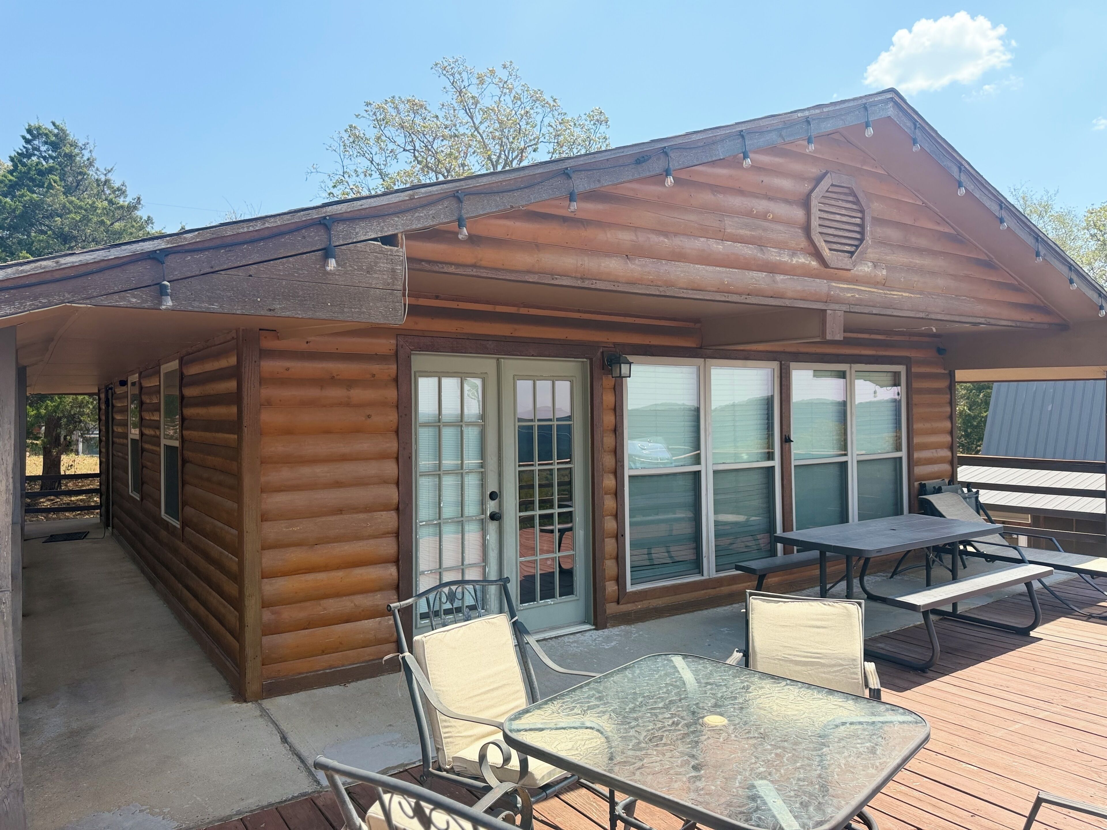 A log cabin with a covered patio, glass doors, and outdoor seating.
