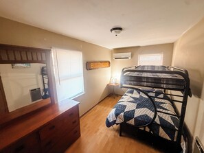 A bunk bed with a quilt, a dresser, a wall-mounted air conditioner, and a sign that reads 'BUNKHOUSE'.