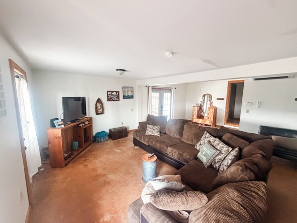 A living room with a large brown sofa, a television, a wooden cabinet, and a mirror.