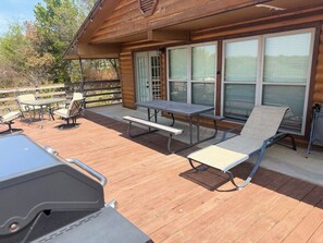 A wooden deck with a barbecue grill, picnic table, and lounge chairs.