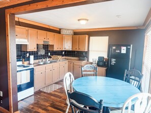 A kitchen with wooden cabinets, a stove, a sink, a refrigerator, and a dining table with chairs.