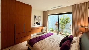 A bedroom with a large bed, a wooden wardrobe, a desk, and a view of greenery outside. - Villa Amara - Viluma Villas (Hua Hin)