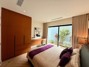 Ein Schlafzimmer mit einem großen Bett, einem Holzschrank, einem Schreibtisch und Blick ins Grüne.