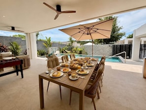 A dining area with a pool view, a table set for a meal, and a ceiling fan. - Villa Amara - Viluma Villas (Hua Hin)