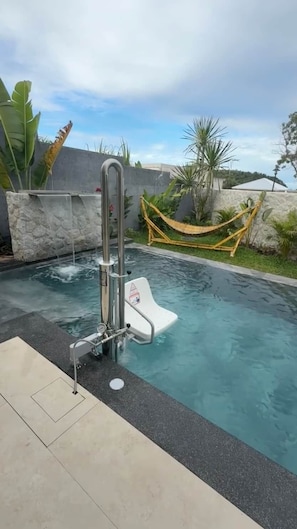 Ein Swimmingpool mit integriertem Wasserspiel, einem weißen Sicherheitsschild und einer Hängematte.