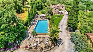 Ein Poolbereich mit Liegestühlen, ein Steinhaus und umliegendes Grün.