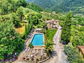 Ein Poolbereich mit Liegestühlen, ein Steinhaus und umliegendes Grün.