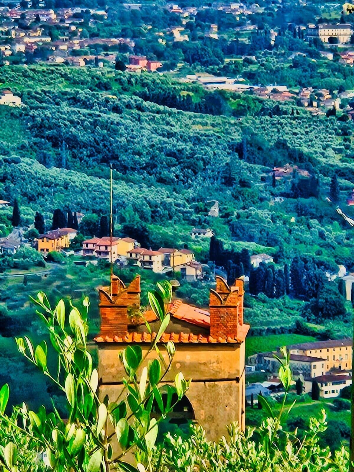 Une vue d’une ville avec un imposant beffroi au premier plan, entouré de verdure et de bâtiments.