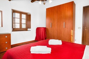 A bedroom with a large wardrobe, a bed with red bedding, a window, and a red chair. - La Marginella, Intera Villa • Toscana • 14 pax (Pescia)