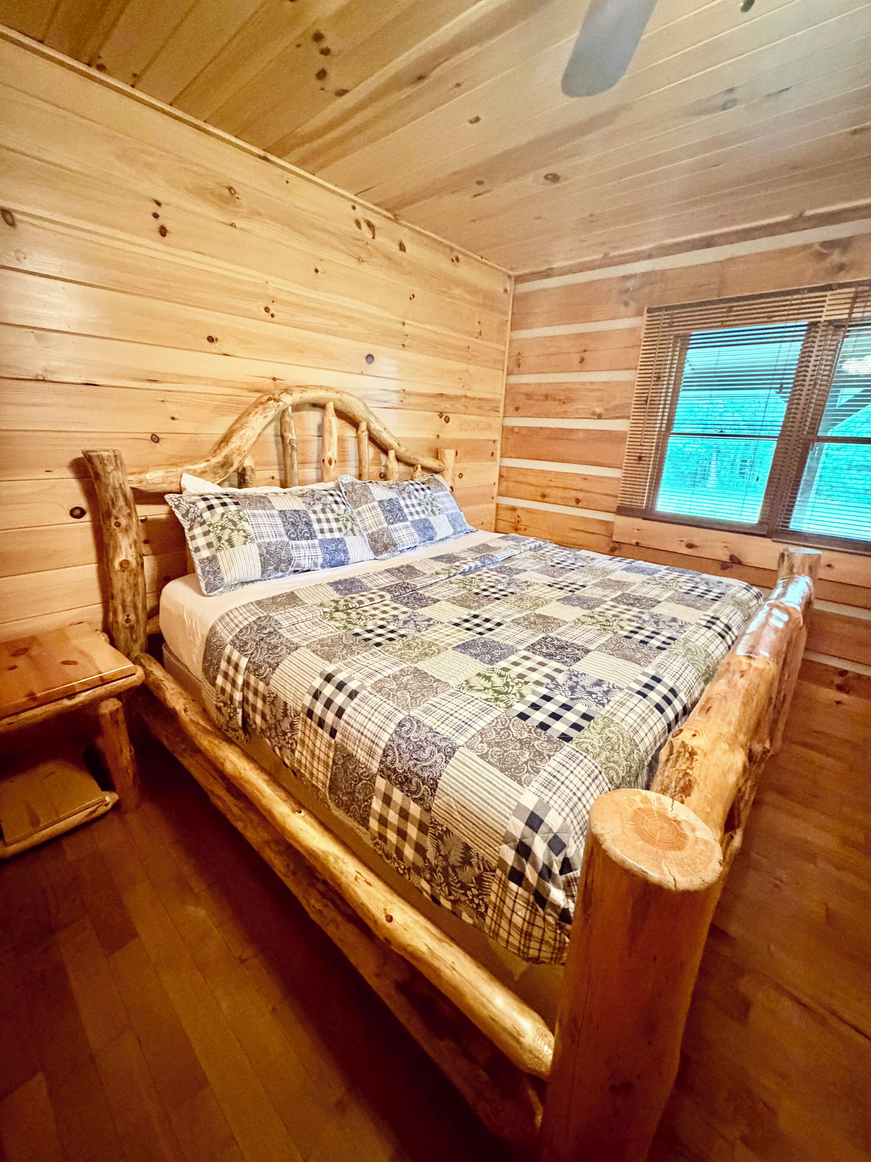 A wooden cabin bedroom with a bed, a nightstand, and a window.