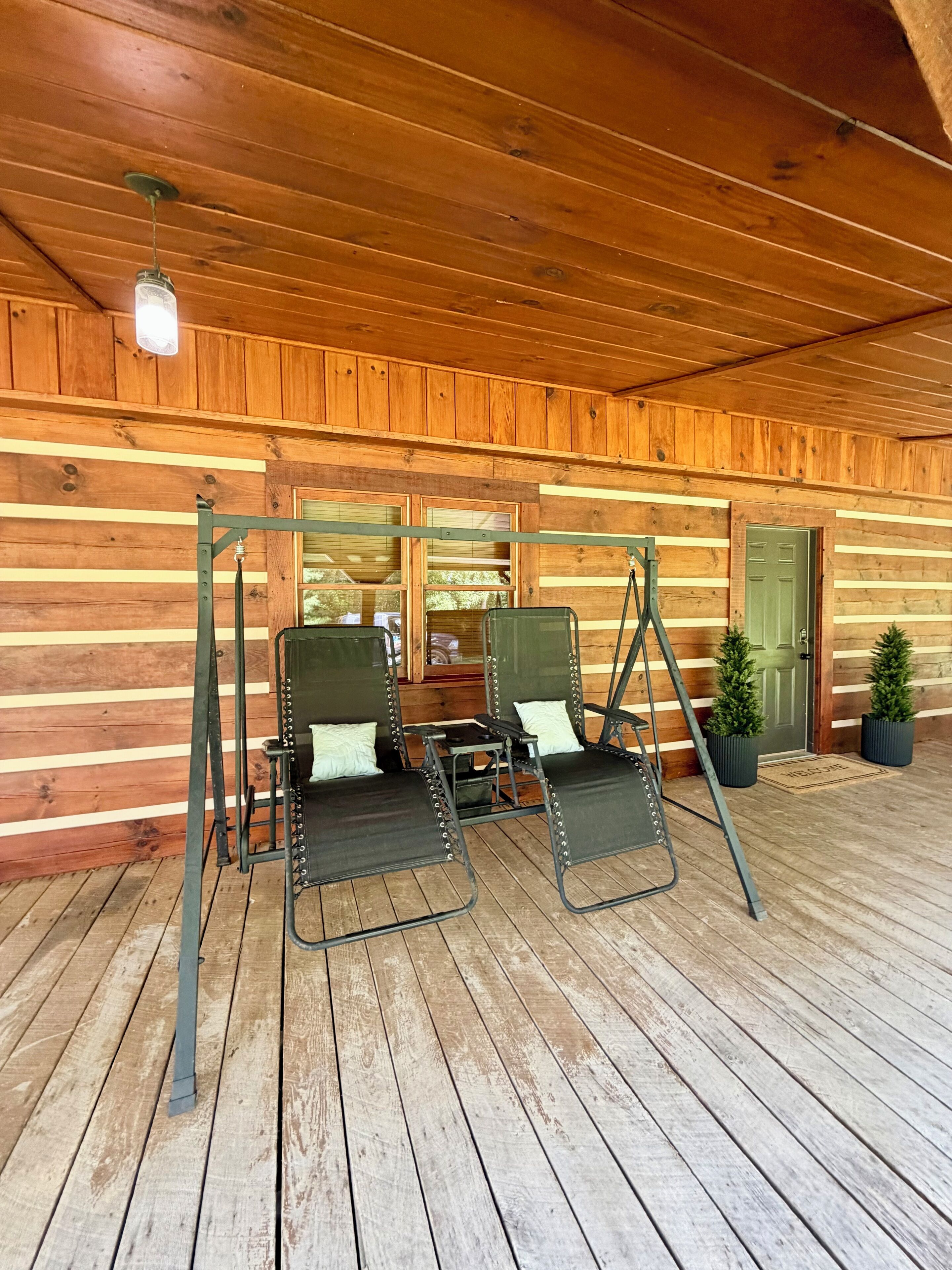 A wooden cabin with a porch, two swing seats, a door, and a window.