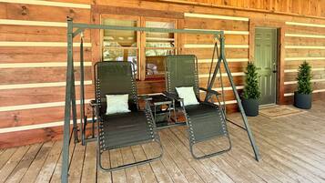 A wooden cabin with a porch, two swing seats, a door, and a window.