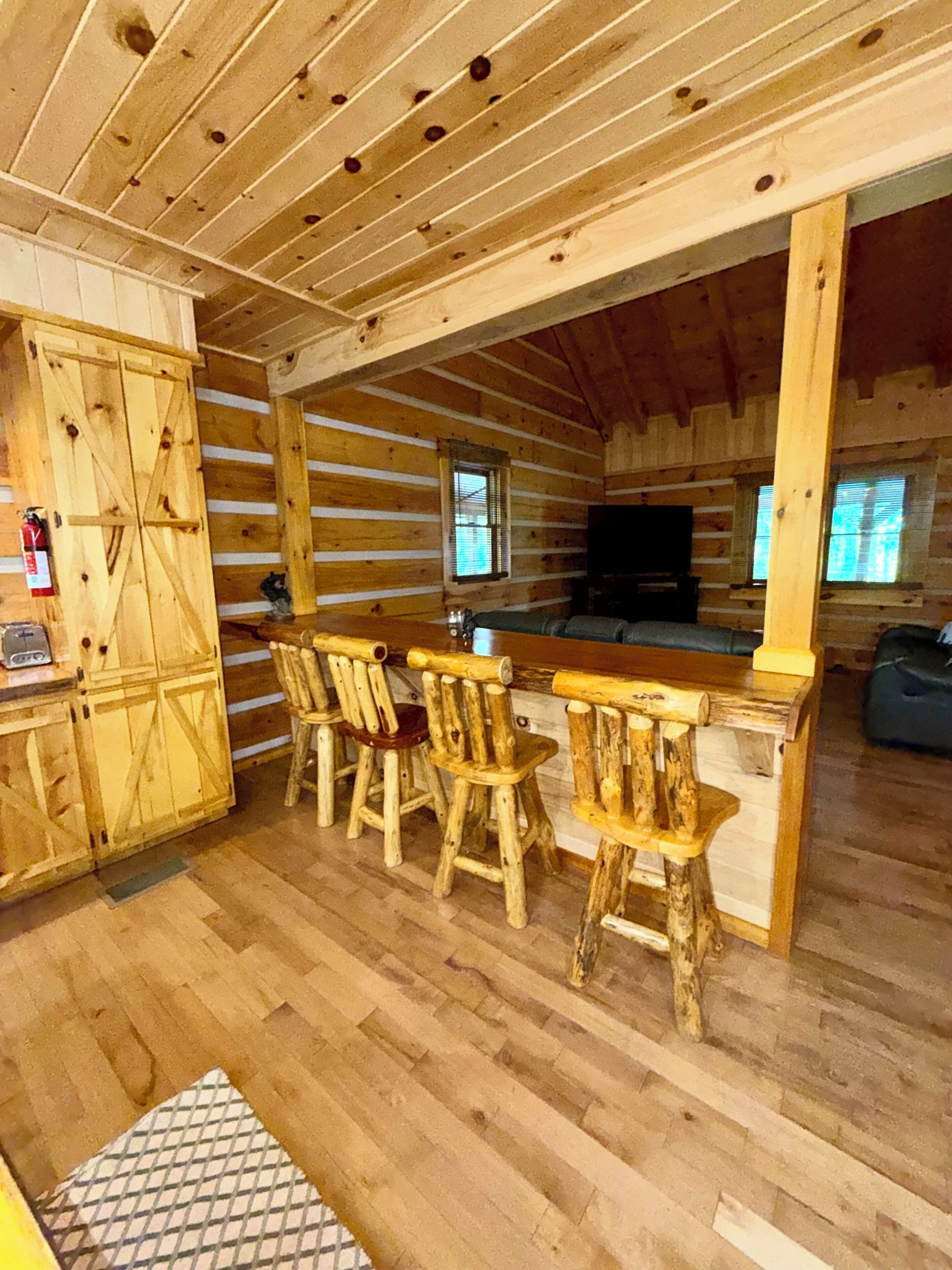 A log cabin interior with a wooden dining area, a kitchen with a television, and a fire extinguisher.