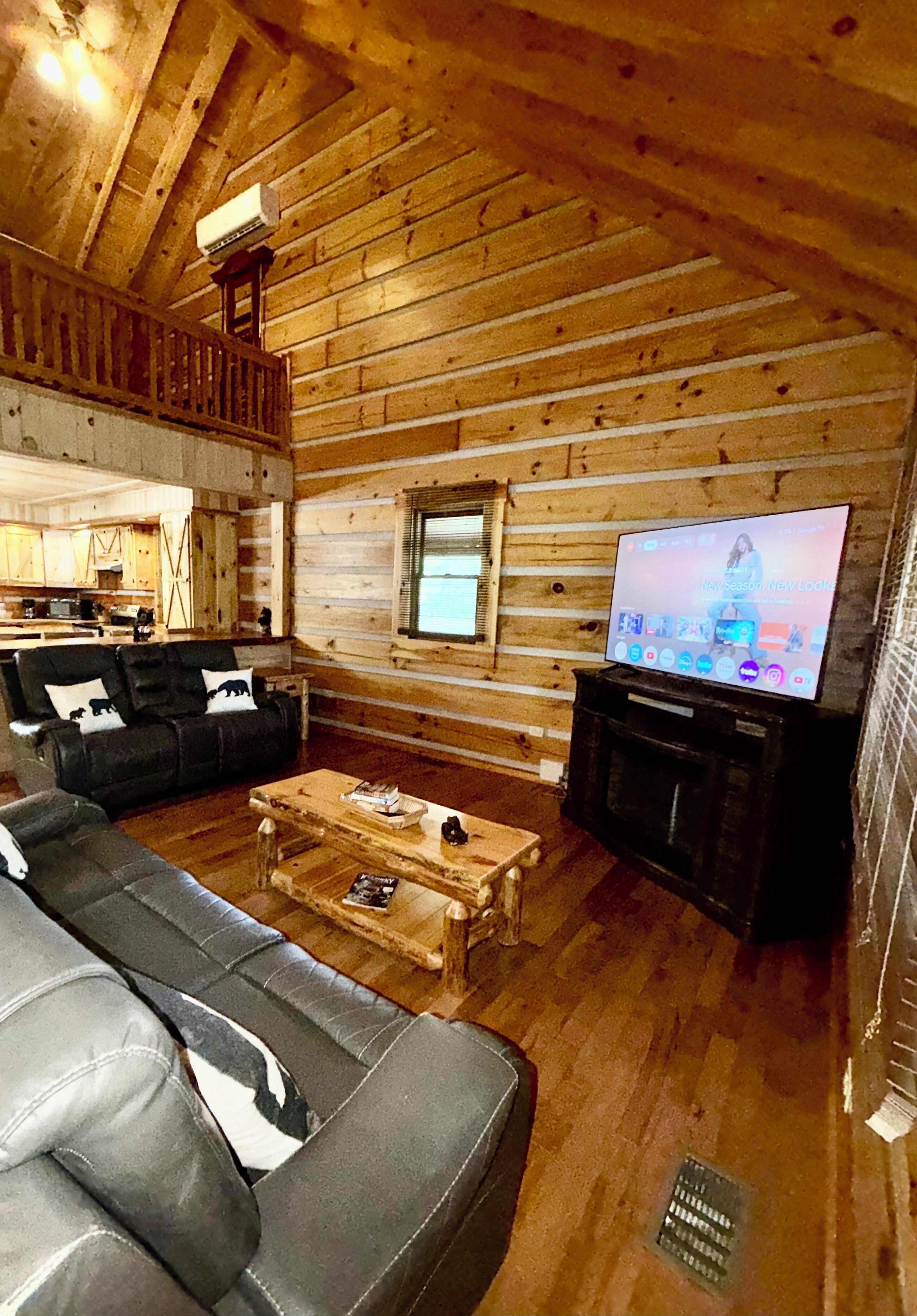 A log cabin interior with a wooden ceiling, a living room with a sofa set, a coffee table, and a television.