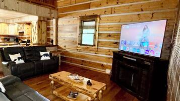 A log cabin interior with a wooden ceiling, a living room with a sofa set, a coffee table, and a television.