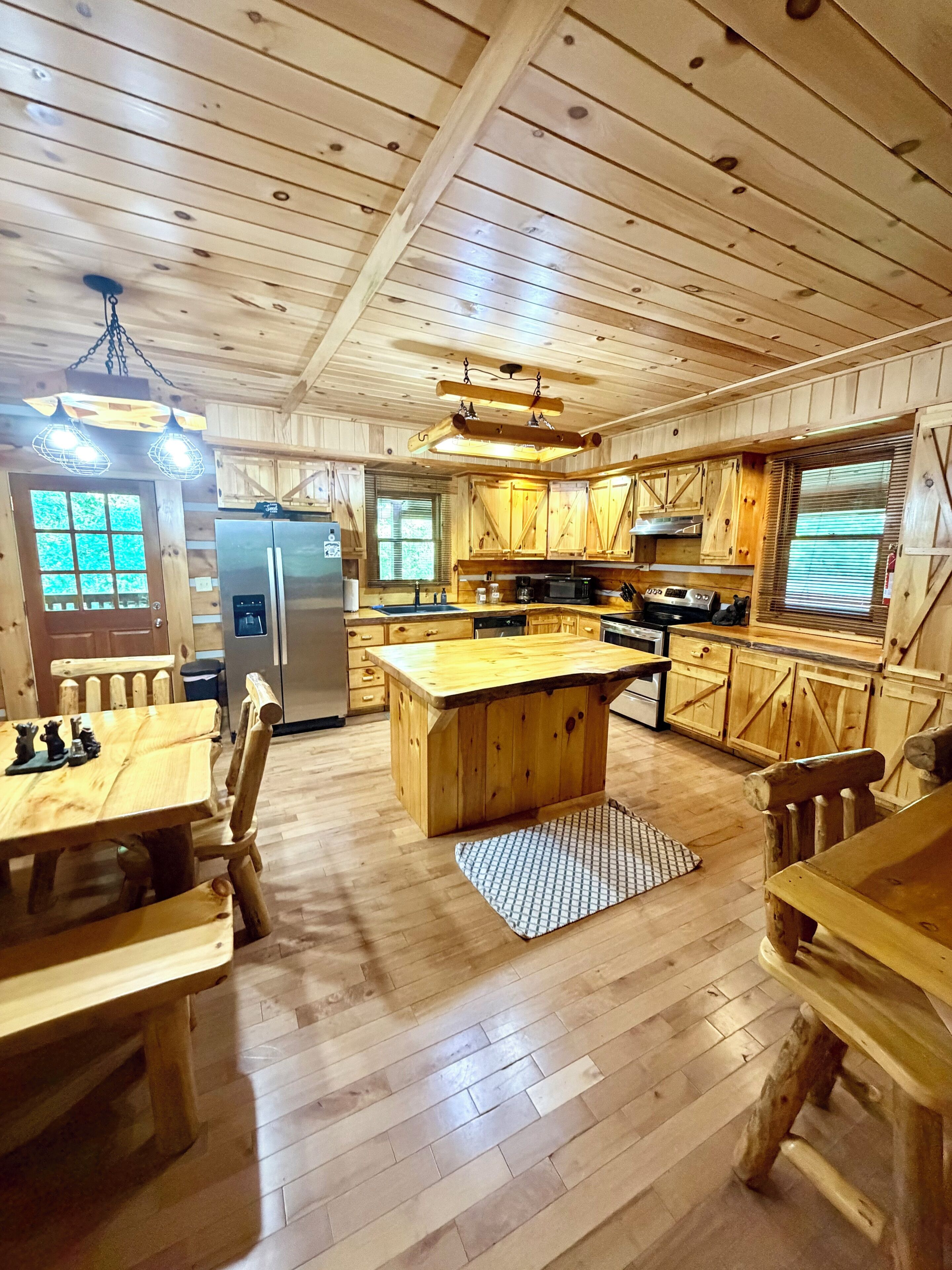 A wooden cabin interior with a kitchen, dining area, and a large window.