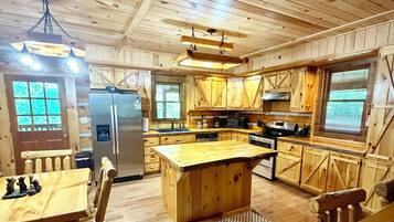 A wooden cabin interior with a kitchen, dining area, and a large window.