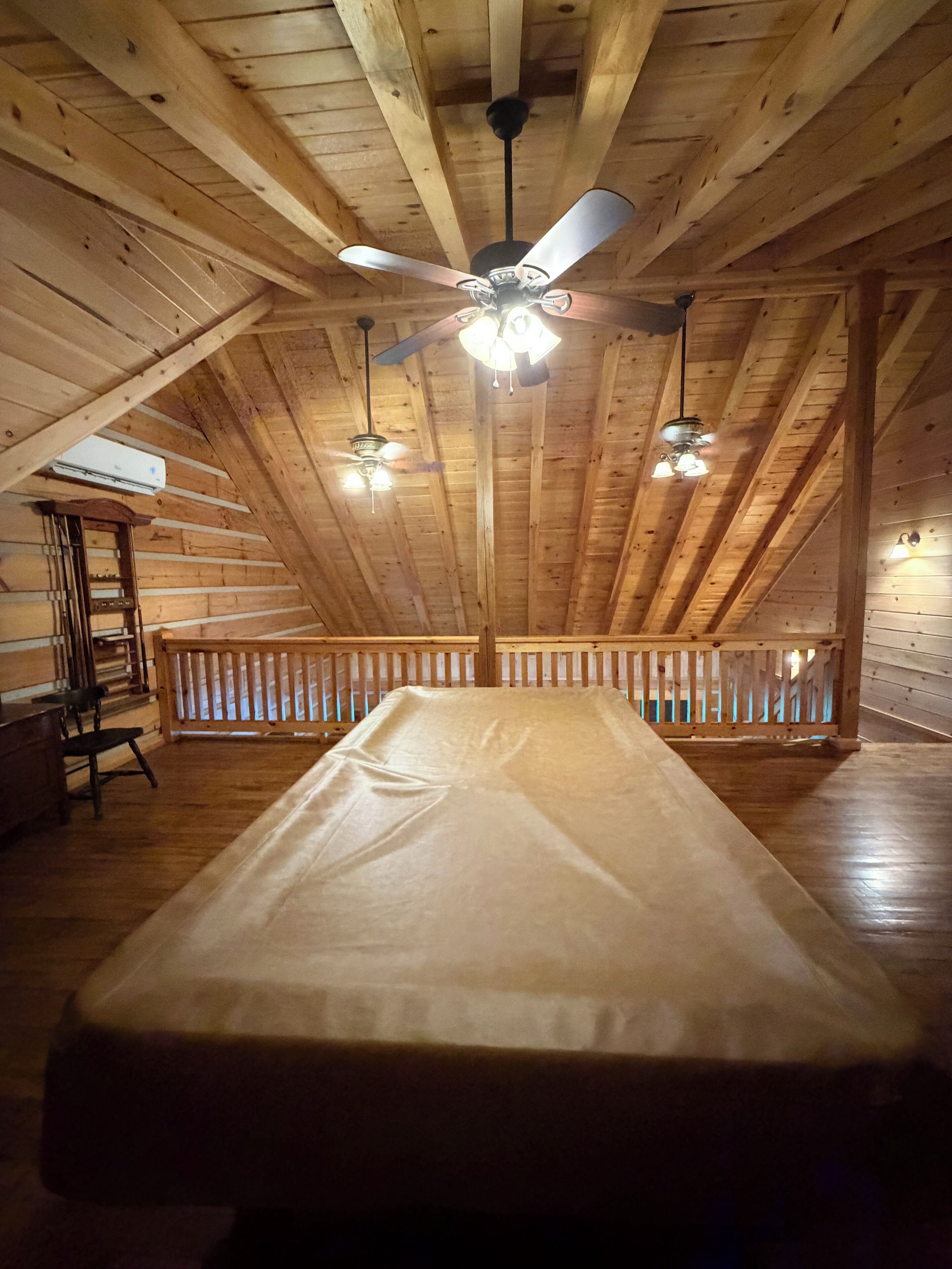 A room with a ceiling fan, an air conditioning unit, a bed, and a wooden railing.