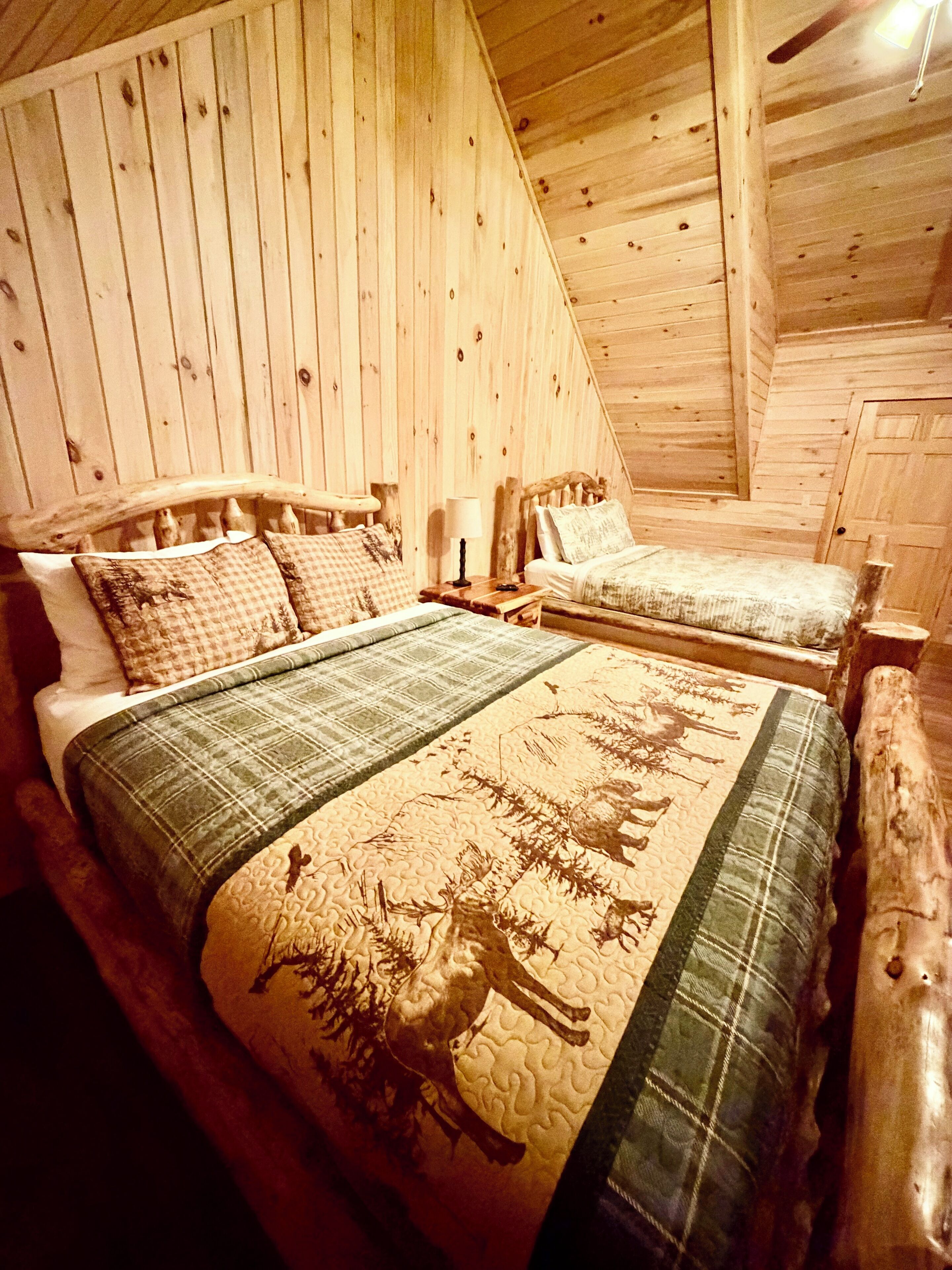 Un dormitorio de cabaña de madera con dos camas, una mesita de noche y una lámpara.