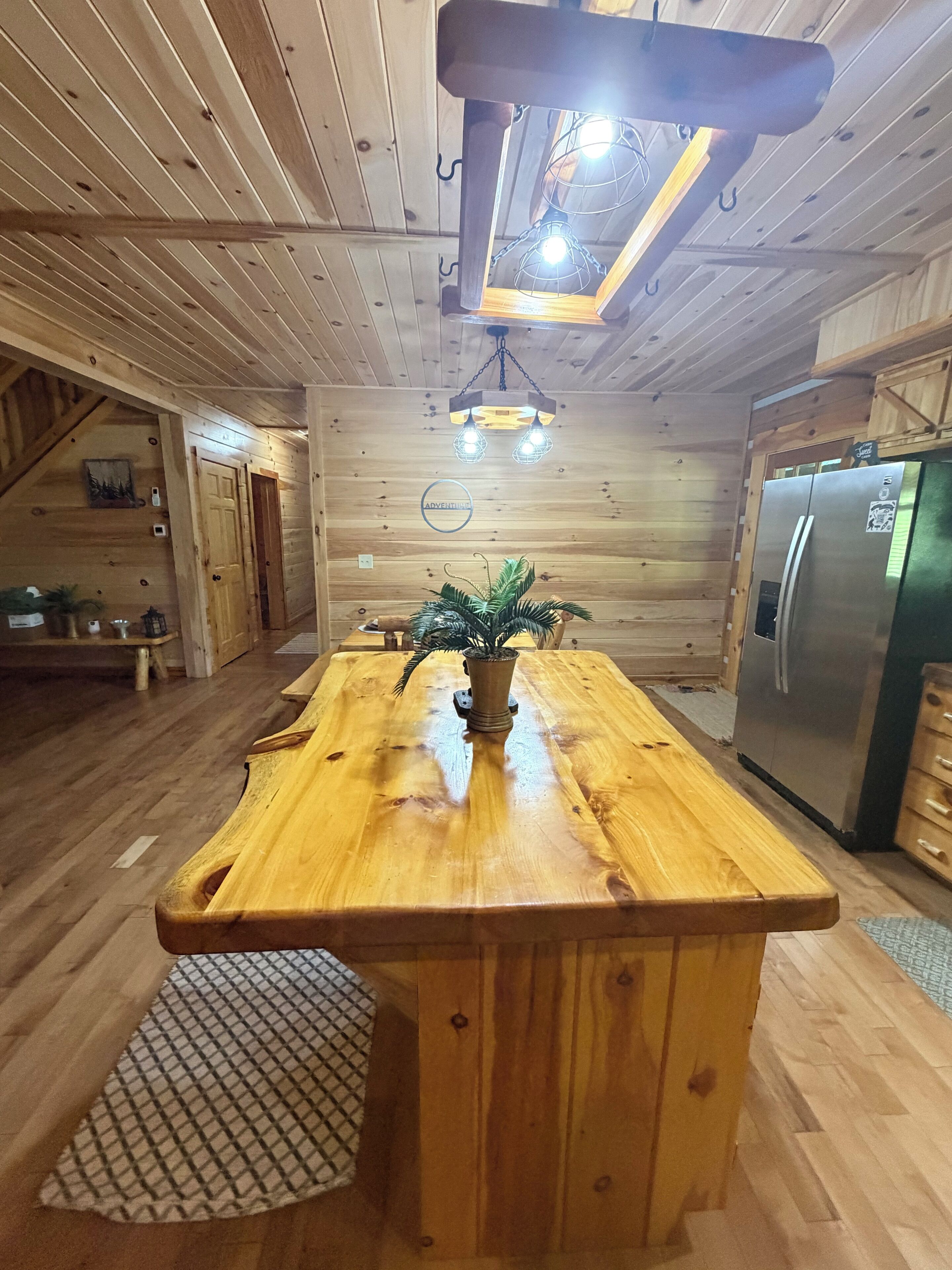 A wooden interior with a central island, a refrigerator, and a hanging light fixture.
