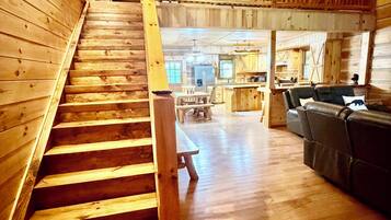 Un intérieur en bois avec un escalier menant à un deuxième étage, un coin repas et un espace salon avec un canapé.