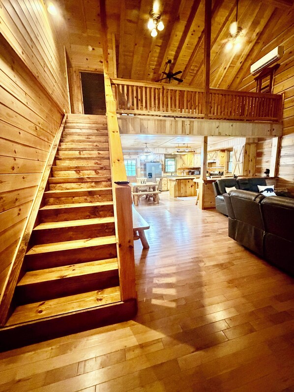 A wooden interior with a staircase leading to a second floor, a dining area, and a seating area with a sofa.