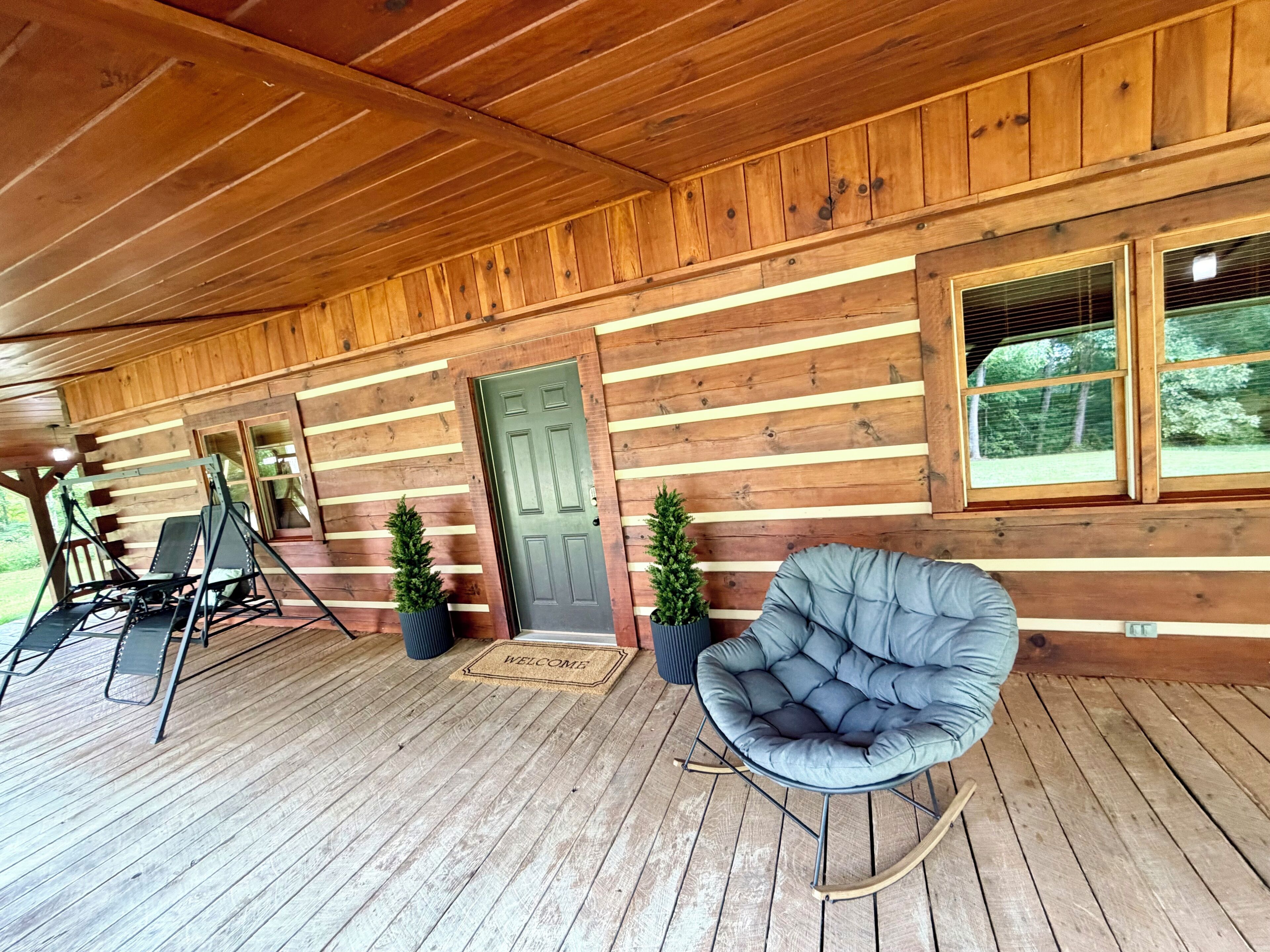 A wooden cabin with a porch, a swing set, a rocking chair, and a door with a welcome mat.