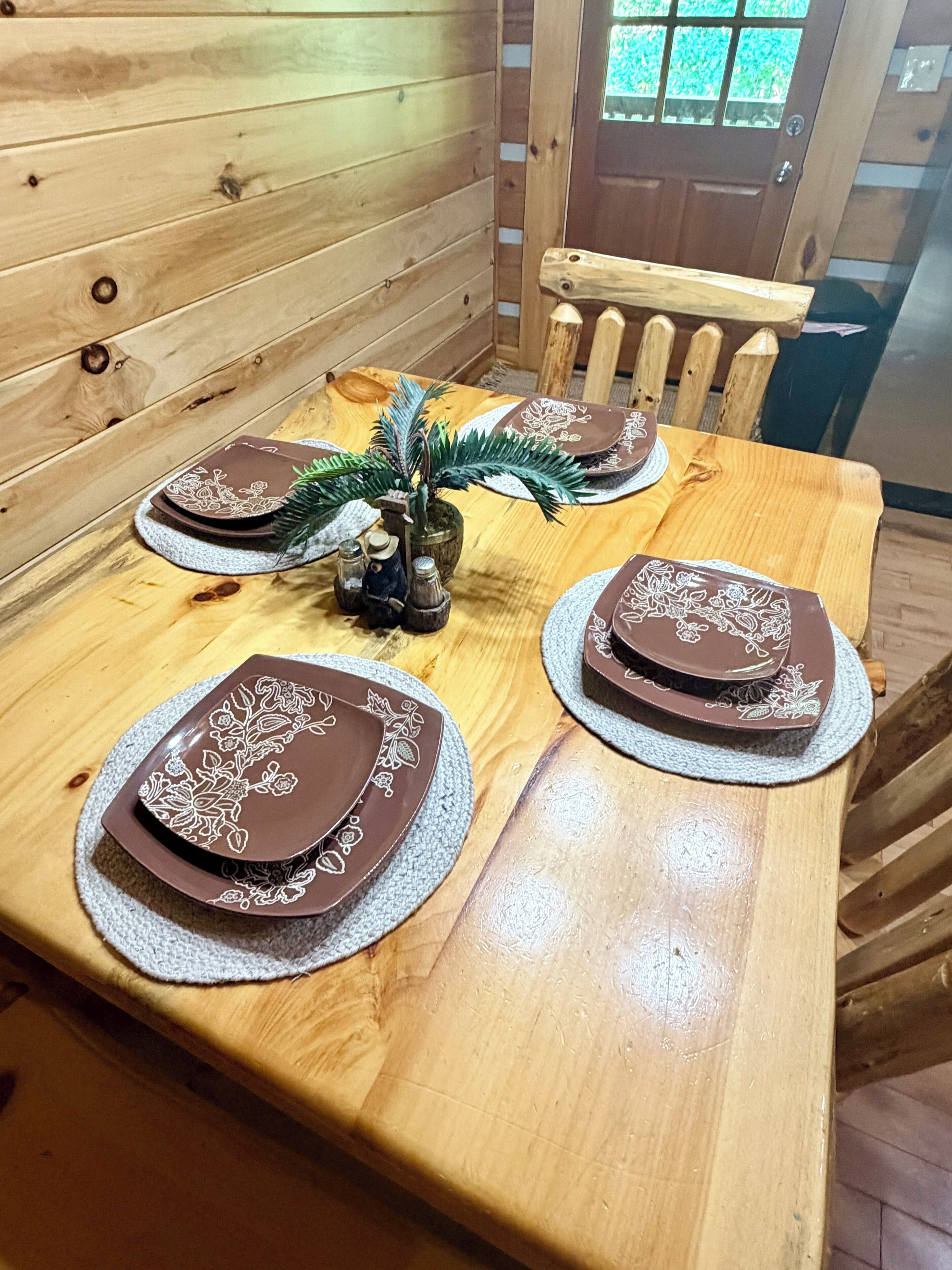 A wooden dining table with four plates, a small plant, and a wooden chair.