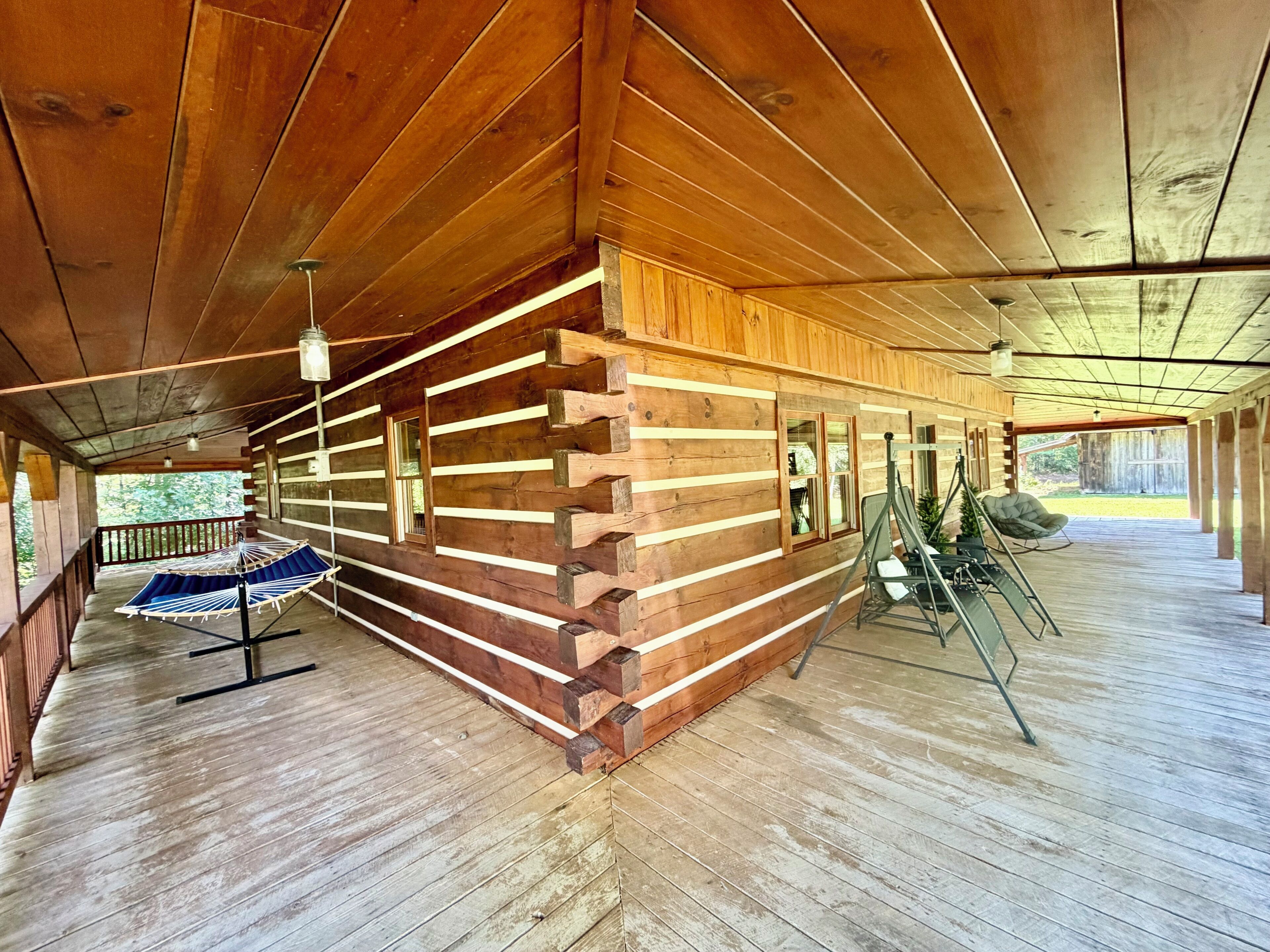 A log cabin with a covered porch, a hammock, and a chair.