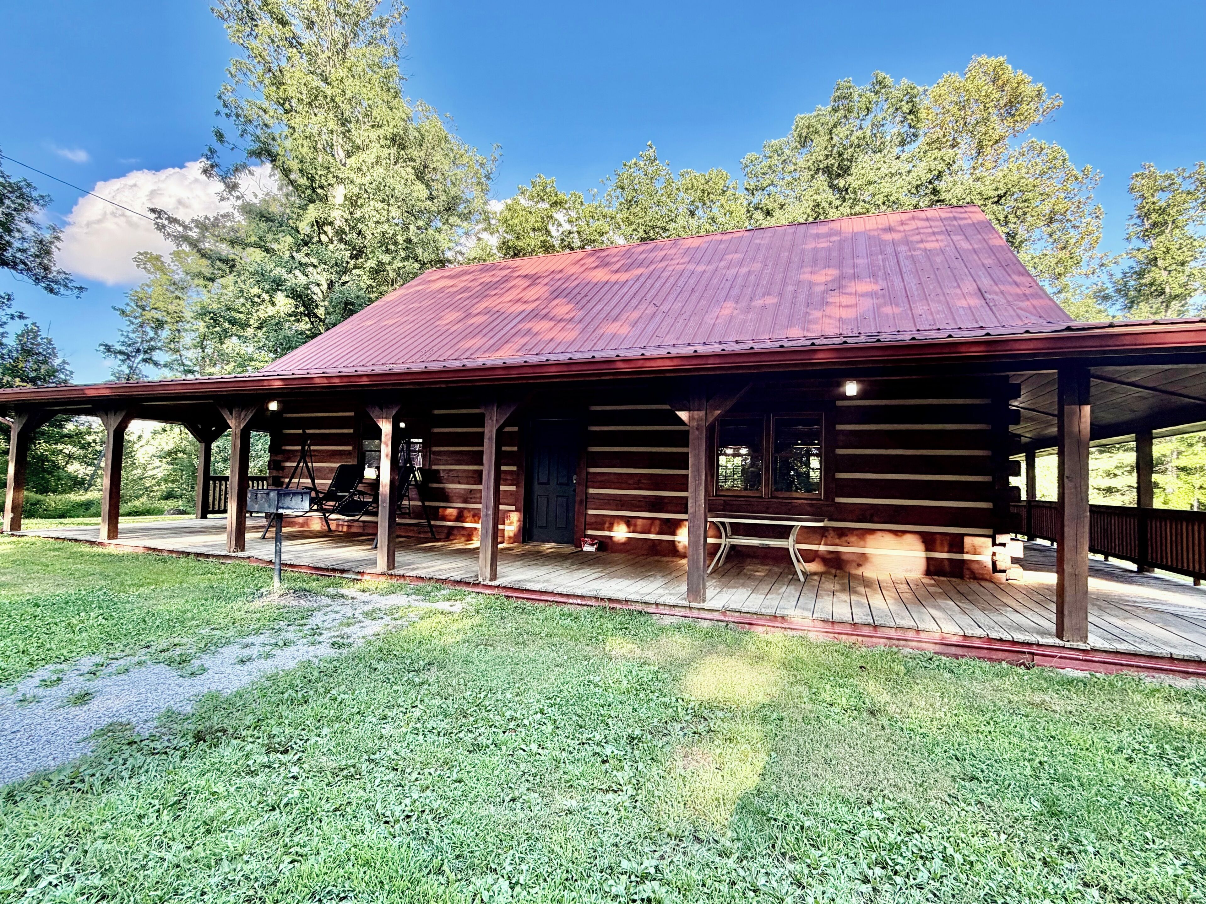A rustic cabin with a porch, wooden deck, and a metal roof.
