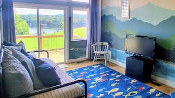 A bedroom with a bed, a TV, and a view of a lake through a sliding door.