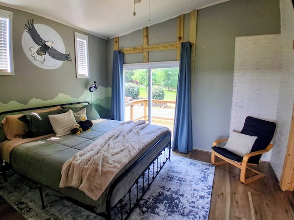 A bedroom with a bed, a chair, a wall mural, and a view through a window.