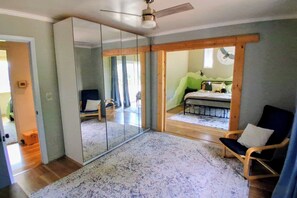 A room with a large sliding glass door leading to a balcony, a bed with a green wall, a chair, and a ceiling fan.