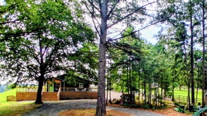 A rustic cabin with a wooden deck, surrounded by a forested area with a gravel path leading to it. - Sunrise over the lake and mountains...  (Albemarle)