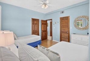Ein Schlafzimmer mit zwei Betten, einem Deckenventilator, Holztüren, einer Kommode und einem Spiegel.