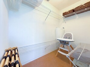 Ein Zimmer mit weißer Wand, einem Metallregal, einer Wickelstation und einem Babysitz.
